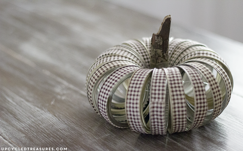 See how easy it is to create this rustic fall mason Jar lid pumpkin using canning lids, fabric tape, fishing line and a stick!